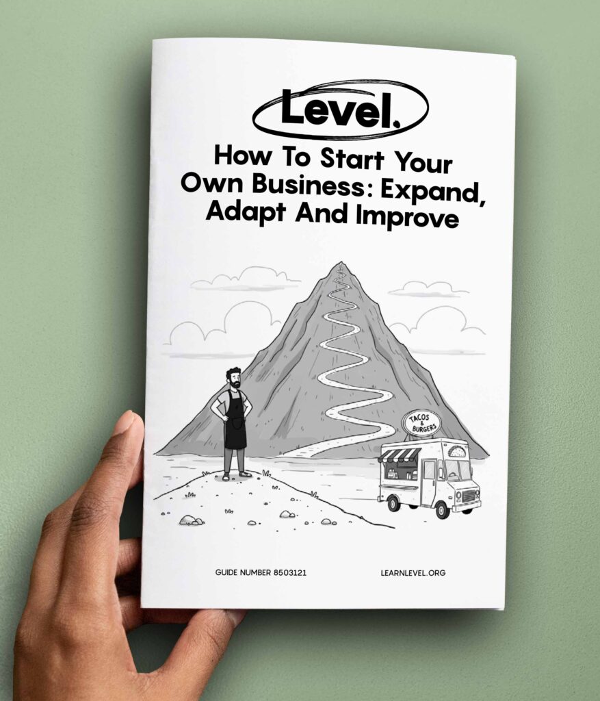 Hand holding a printed version of Level's prison education guide How To Start Your Own Business: Expand, Adapt And Improve